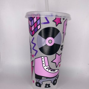 May include: A grey reusable cup with a pink, purple and black retro design. The design includes a roller skate, a record, a star, a lightning bolt and a geometric pattern.