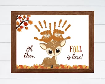 Puede incluir: Impresión enmarcada con un ciervo de dibujos animados y astas con forma de huellas de manos. El texto "Oh Deer, FALL is here!" se muestra con hojas de otoño. El marco es de color marrón oscuro.