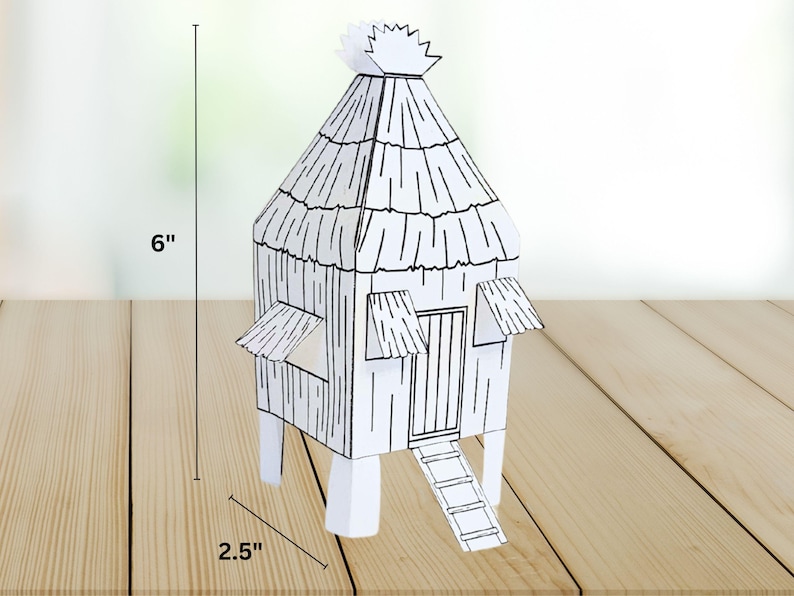 May include: A black and white paper model of a thatched-roof hut, approximately 6 inches tall and 2.5 inches wide. The hut features a door, a ladder, and two small awnings. The model is set on a wooden surface.