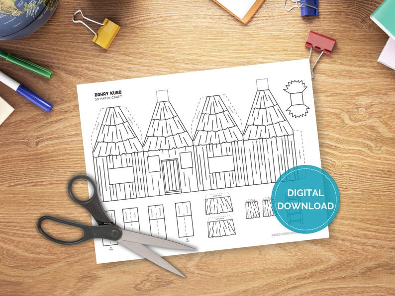 May include: A black and white paper craft template labeled "Bahay Kubo 3D Paper Craft" featuring a house design. Scissors and office supplies are on a wooden desk. A blue circle with the words "DIGITAL DOWNLOAD" is on the paper.