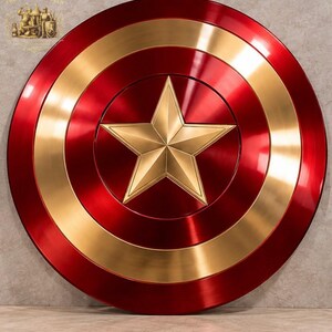 Pode incluir: Um escudo circular com acabamento metálico vermelho e dourado, apresentando uma estrela dourada de cinco pontas proeminente no centro. O design consiste em anéis concêntricos alternados de metal polido vermelho e dourado, criando reflexos.