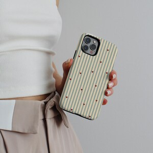 May include: A phone case with a striped pattern in beige and gray, adorned with small red hearts. The case has a black border and a camera cutout. The design is simple and elegant, suitable for everyday use.