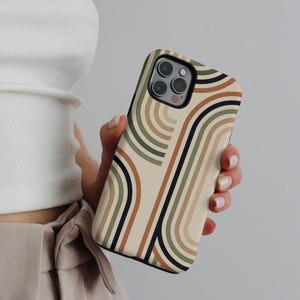 May include: A phone case with a retro-inspired design. The case features a pattern of curved lines in shades of beige, brown, green, and black. The phone case is held in a person's hand, showcasing the design and the phone's camera.