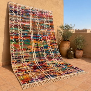 May include: A rectangular area rug featuring a vibrant, multi-colored horizontal striped pattern with interspersed white geometric diamond lines. The rug is finished with a cream-colored fringe along the bottom edge and has a textured, woven surface.