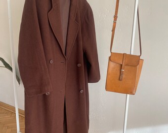 May include: A long brown wool coat with a double breasted closure and a brown leather shoulder bag.