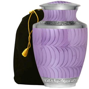 May include: A lavender cremation urn with a silver lid and a silver band around the middle. The urn has a wavy pattern and is decorated with a silver floral design. It comes with a black velvet bag with a gold drawstring.