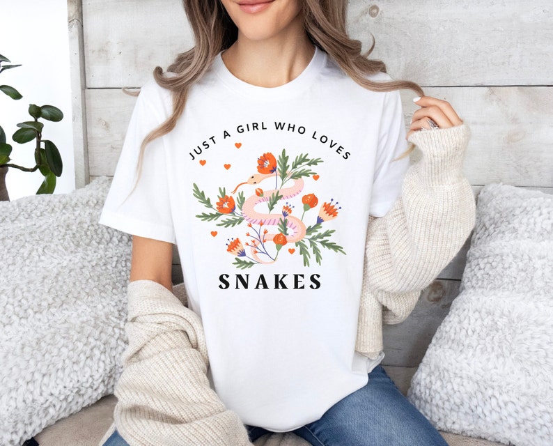 May include: White t-shirt with a floral design and a pink snake. The text "Just a girl who loves snakes" is printed on the shirt.
