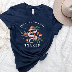 May include: A navy blue t-shirt with a graphic of a pink snake with red flowers and the text "Just a girl who loves snakes".