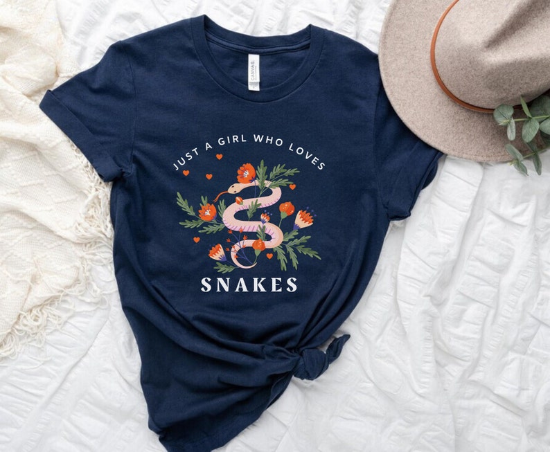 May include: A navy blue t-shirt with a graphic of a pink snake with red flowers and the text "Just a girl who loves snakes".