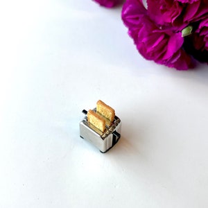 May include: A miniature silver toaster with two slices of bread inside. The toaster is on a white surface.