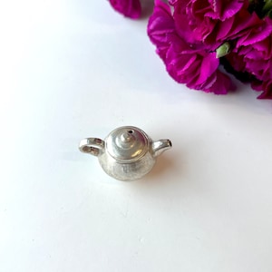 May include: A small silver teapot with a rounded body and a spout. The teapot is sitting on a white surface.