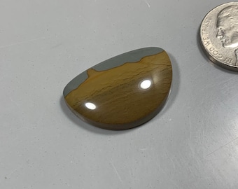 May include: A polished, oval-shaped cabochon gemstone with a gray and brown pattern. The stone has a smooth, glossy finish.
