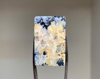 May include: A rectangular, white, black, and yellow agate cabochon with a dendritic pattern. The cabochon is set in a metal frame.