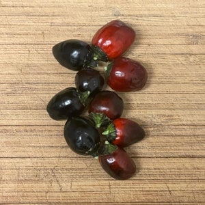 May include: A group of seven small peppers, some red and some black, arranged on a wooden surface.