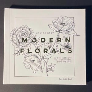 May include: A white book titled "How to Draw Modern Florals" with black line drawings of flowers. The book cover includes text: "An introduction to the art of flowers, cacti, and more" and "By: Alli Koch".
