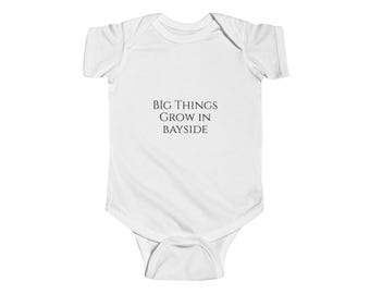Puede incluir: Un body blanco para bebé con mangas cortas y cierre a presión. El body tiene texto negro que dice "BIG THINGS GROW IN BAYSIDE".