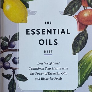 May include: A book cover with the title "The Essential Oils Diet". The cover features a white bottle-shaped design with text and illustrations of lemons, oranges, and other fruits and leaves. The book promises to help readers lose weight and transform their health.