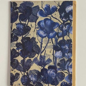 May include: Greeting card featuring a floral design with navy blue flowers on a beige background. The flowers have a watercolor effect, with dark blue details and stems. The card has a natural brown border.