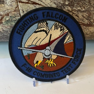 May include: A blue and white embroidered patch with the text "Fighting Falcon F.E.B. Combined Test Force" and a stylized image of a falcon.