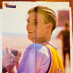 May include: A vintage poster showing a person smiling and wearing a yellow and white jersey with the name "Jove" on the back. The poster has the "16/nick" logo. The person is holding a football.