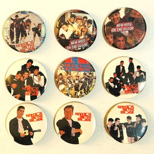 May include: Nine round buttons featuring images of the band New Kids on the Block. Each button has a different image of the band members, with the band's name printed on each button. The buttons are white with a glossy finish.