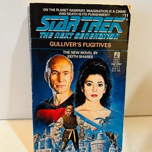 Puede incluir: Un libro de bolsillo vintage titulado "Star Trek: The Next Generation: Gulliver's Fugitives" de Keith Sharee. La portada presenta retratos de dos personas y una figura con atuendo medieval, sobre un fondo azul con el texto "On the planet Rampart, imagination is a crime and death is its punishment!"