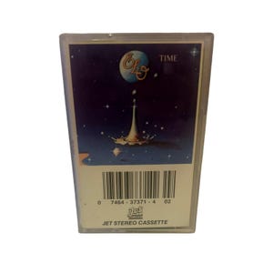 Può includere: Una custodia per cassette con un'immagine blu e bianca di un pianeta con una goccia d'acqua che cade su di esso. Il testo "ELO" e "TIME" sono stampati sulla custodia. Il codice a barre e il testo "JET STEREO CASSETTE" sono stampati sul fondo della custodia.