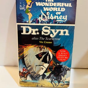 May include: A vintage paperback book titled "Dr. Syn alias The Scarecrow" from "The Wonderful World of Disney." The cover features a scarecrow illustration and a scene of riders on horseback. A red sticker reads "NOW A WALT DISNEY FEATURE FILM!"