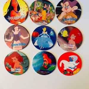 Könnte beinhalten: Neun runde Disney-Untersetzer mit Charakteren wie Pocahontas, Schneewittchen, Cinderella, Arielle und Dumbo. Jeder Untersetzer hat eine farbenfrohe Illustration und das Disney-Logo. Die Untersetzer liegen auf einer weißen Oberfläche.