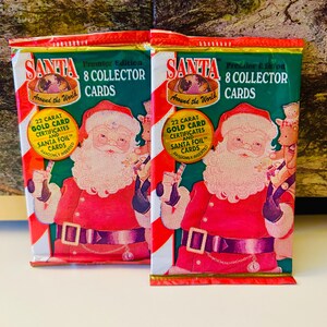 May include: Two unopened packs of "Santa Around the World" collector cards. Each pack features a red and white design with an illustration of Santa Claus. Text includes "8 Collector Cards" and "22 Carat Gold Card Certificates."