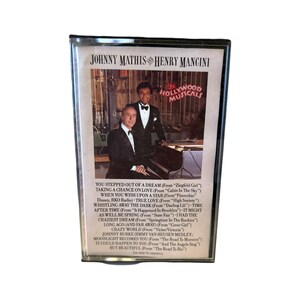May include: A black and white cassette tape case featuring a photo of Johnny Mathis and Henry Mancini. The case includes the text "Hollywood Musicals" and lists songs from the album.