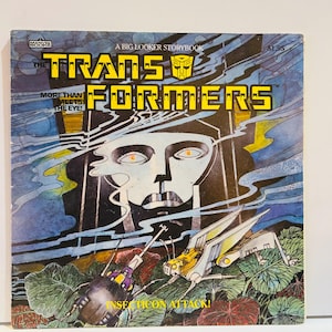 Op de afbeelding: Vintage Transformers stripboekcover, getiteld "A Big Looker Storybook". De cover heeft een gele titel en een robotgezichtillustratie. De illustratie toont een gevechtsscène met insectachtige robots en de tekst "Insecticon Attack!"