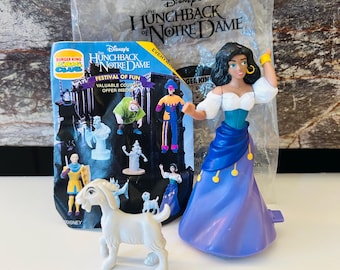 May include: A Disney's Hunchback of Notre Dame Burger King toy set. The set includes a figure of Esmeralda in a blue and purple dress, a white goat, and a promotional package. The package features various character figures.