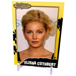 May include: A yellow and black trading card with a photo of Elisha Cuthbert. The card has a black and white palm tree design in the background and the text "POPCARDZ" in a yellow star.