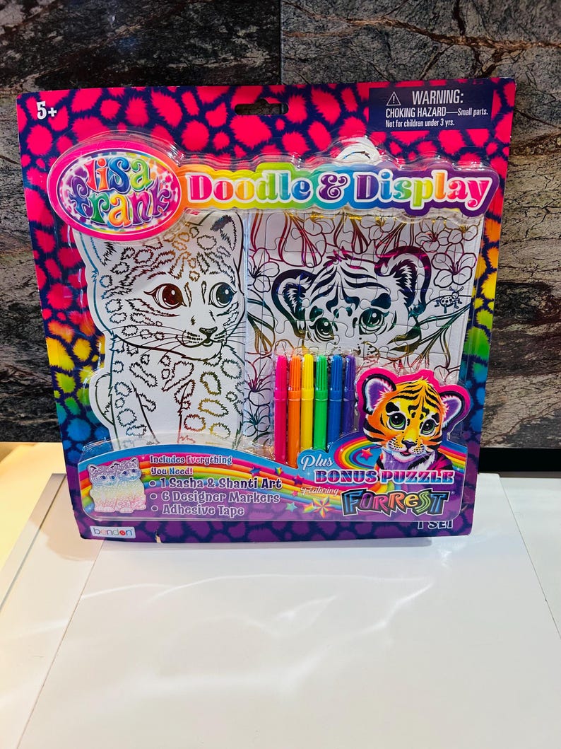 May include: A Lisa Frank Doodle & Display art kit. The package features a pink and blue leopard print design. The kit includes Sasha & Shanti art, 6 designer markers, and adhesive tape. A bonus puzzle is also included.