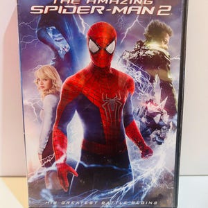 May include: DVD case for "The Amazing Spider-Man 2" movie. The cover features Spider-Man in a red and blue suit, with other characters and lightning effects. The text "HIS GREATEST BATTLE BEGINS" is at the bottom.