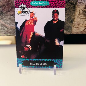 Op de afbeelding: Een vintage Bell Biv DeVoe-verzamelkaart uit de ProSet Musicards-serie. De kaart toont een foto van de muziekgroep met het "Yo! MTV Raps"-logo. De kaart wordt weergegeven op een transparante plastic standaard.