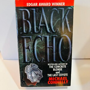 May include: A paperback book titled "The Black Echo" by Michael Connelly. The cover features the title in large, stylized letters, a police badge, and the text "Edgar Award Winner". The background is dark with a textured appearance.