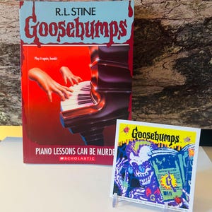 May include: A hardcover book and a trading card featuring the title "Goosebumps." The book cover is red and blue, with the title in large, dripping letters. The trading card shows a skeleton reading a book. The book title is "Piano Lessons Can Be Murder."