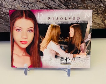 Pode incluir: Um cartão de troca com Dawn do programa de televisão Buffy, a Caça-Vampiros. O cartão é do conjunto de cartões de troca "Buffy, a Caça-Vampiros". O cartão tem um fundo rosa com as palavras "Dawn Resolved" impressas nele. O cartão apresenta uma foto de Dawn no lado esquerdo do cartão e uma foto de Dawn e Buffy no lado direito do cartão.