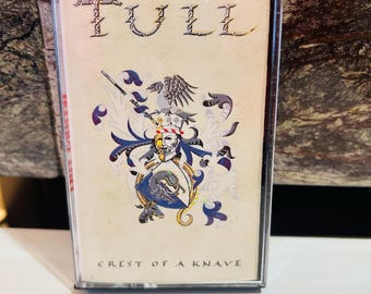 以下が含まれることがあります： ジェスロ・タル「Crest of a Knave」のカセットテープ。透明なカセットケースには、バンド名とアルバムタイトルが様式化されたフォントで表示され、青、金、白の紋章デザインが施されたカバーアートが特徴です。