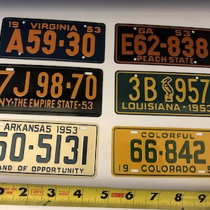 May include: Six vintage license plates from different states, including Virginia, Georgia, New York, Arkansas, Louisiana, and Colorado. The plates are all from the 1950s and feature various colors and designs.