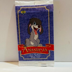 Puede incluir: Un paquete sellado de cromos de "Anastasia". El paquete tiene un fondo morado con un patrón repetido y una imagen de dibujos animados de un perro. La palabra "Anastasia" está en rojo sobre una pancarta roja. El paquete también dice "5 Cromos".