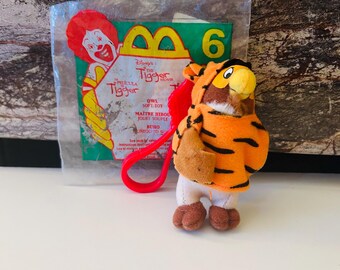 Könnte beinhalten: Ein kleines Plüschtier einer Eule in einem Tigerkostüm mit orangefarbenen und schwarzen Streifen. Das Spielzeug ist an einer roten Schlaufe befestigt und befindet sich in einer transparenten Plastiktüte mit einem McDonald's-Logo und Text aus Disneys Tigger-Film.