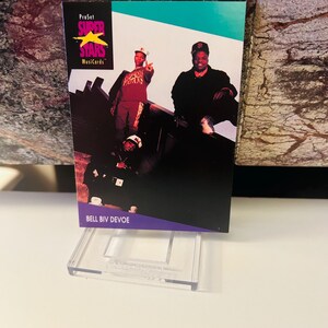 Op de afbeelding: Een Bell Biv DeVoe-verzamelkaart uit de ProSet Super Stars MusiCards-serie. De kaart bevat een foto van de muziekgroep met een zwarte en paarse rand. De kaart wordt weergegeven in een transparante acrylstandaard.
