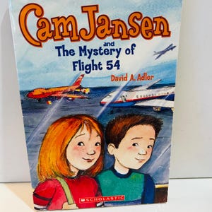 May include: A paperback book titled "Cam Jansen and The Mystery of Flight 54" by David A. Adler. The cover features illustrations of two children, airplanes, and the Scholastic logo.