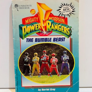 May include: A vintage paperback book titled "Mighty Morphin Power Rangers: The Bumble Beast." The cover features the Power Rangers in their signature colors, with the title in bold, 3D lettering. The book is by Harriet Grey.