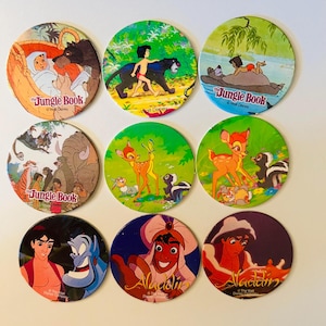 May include: Nine colorful, circular Disney character collectibles. The top row features scenes from "The Jungle Book." The middle row showcases "Bambi." The bottom row displays "Aladdin" characters. Each collectible has a different image and the Disney logo.