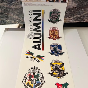 Puede incluir: Una lámina de calcomanías de pared de Harry Potter con el escudo de Hogwarts, emblemas de las casas Gryffindor, Slytherin, Hufflepuff y Ravenclaw, e imágenes de Quidditch. La lámina también incluye el texto "Hogwarts Alumni".