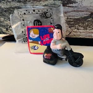 May include: A vintage Fox Kids "Life with Louie" toy figure on a black motorcycle. The figure is a cartoon character with a gray shirt and black hair. A "Jack's Kids Meal" bag and card are in the background.